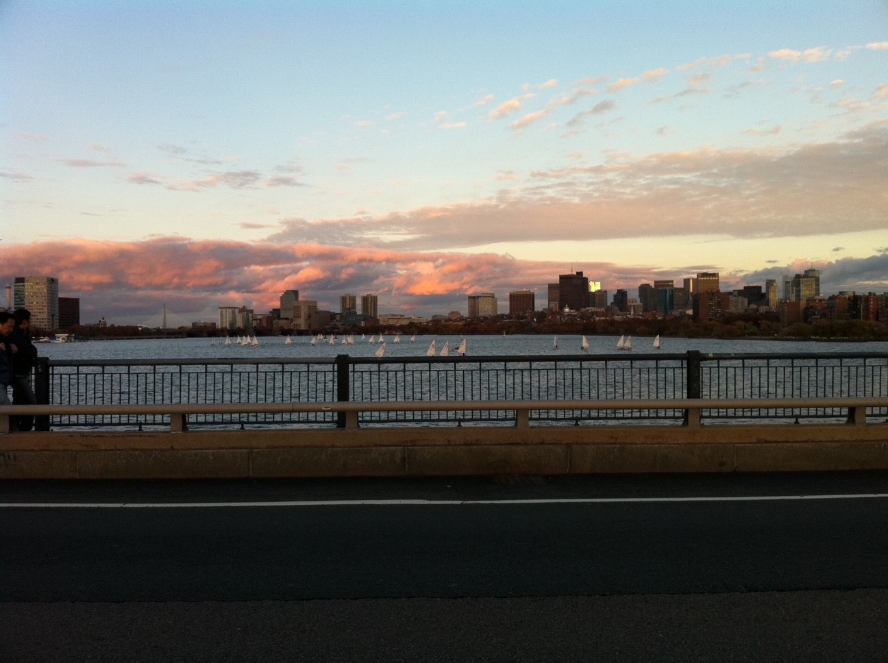 Sunset over a city skyline across a river with a railing in the foreground.